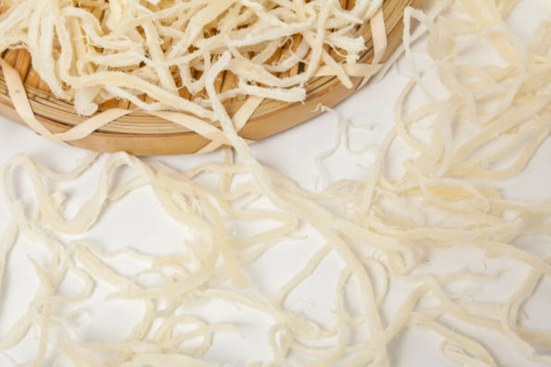 Shredded white oyster mushrooms displayed on a wooden cutting board and white surface, showing their delicate, stringy texture that resembles pulled seafood or noodles, ready for cooking or meal preparation