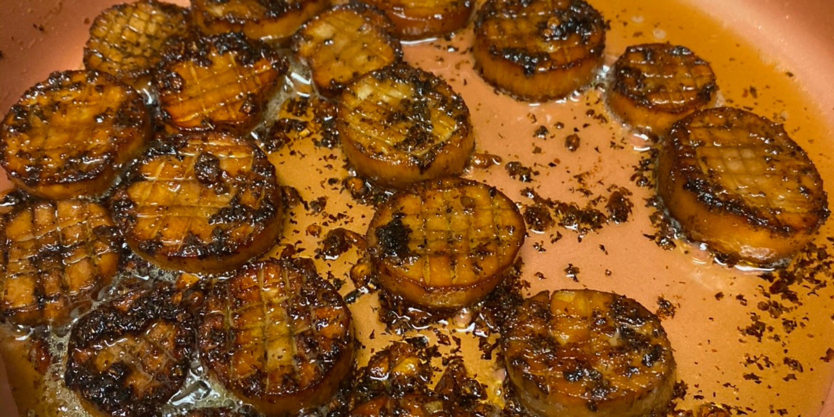 Golden-brown seared king oyster mushroom scallops with crosshatch scoring glistening in butter and black pepper in a copper-colored skillet, displaying caramelized edges and a glossy herb-infused pan sauce.