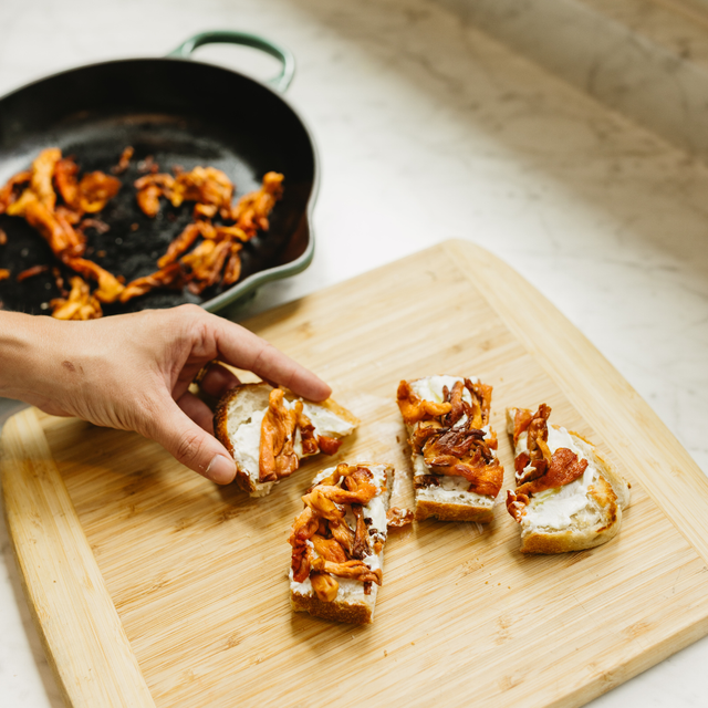 Person preparing a toast with fried pink oysters on a wooden cutting board.