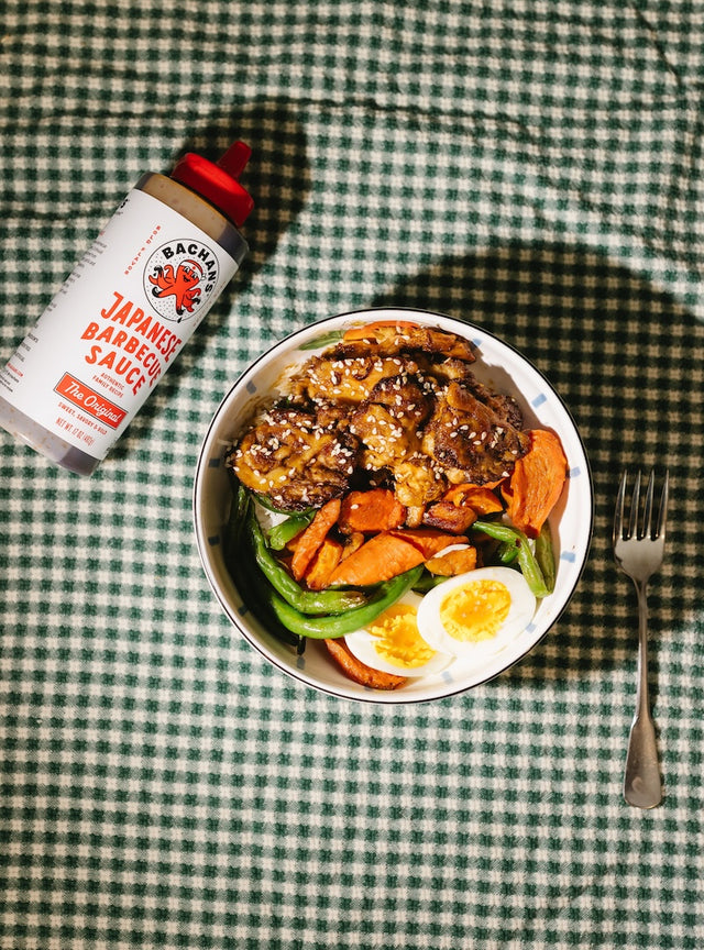 Bowl of food with a can of Backyard lion's mane Japanese Barbecue Sauce on a green checkered tablecloth.
