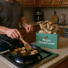 Person cooking Black King Oyster Mushrooms in a pan with a ShroomBag in the background
